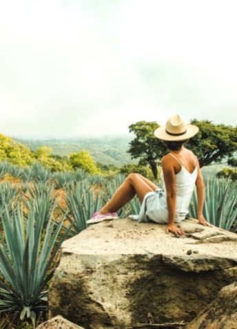 A woman sitting on top of a rock in a desert prairie